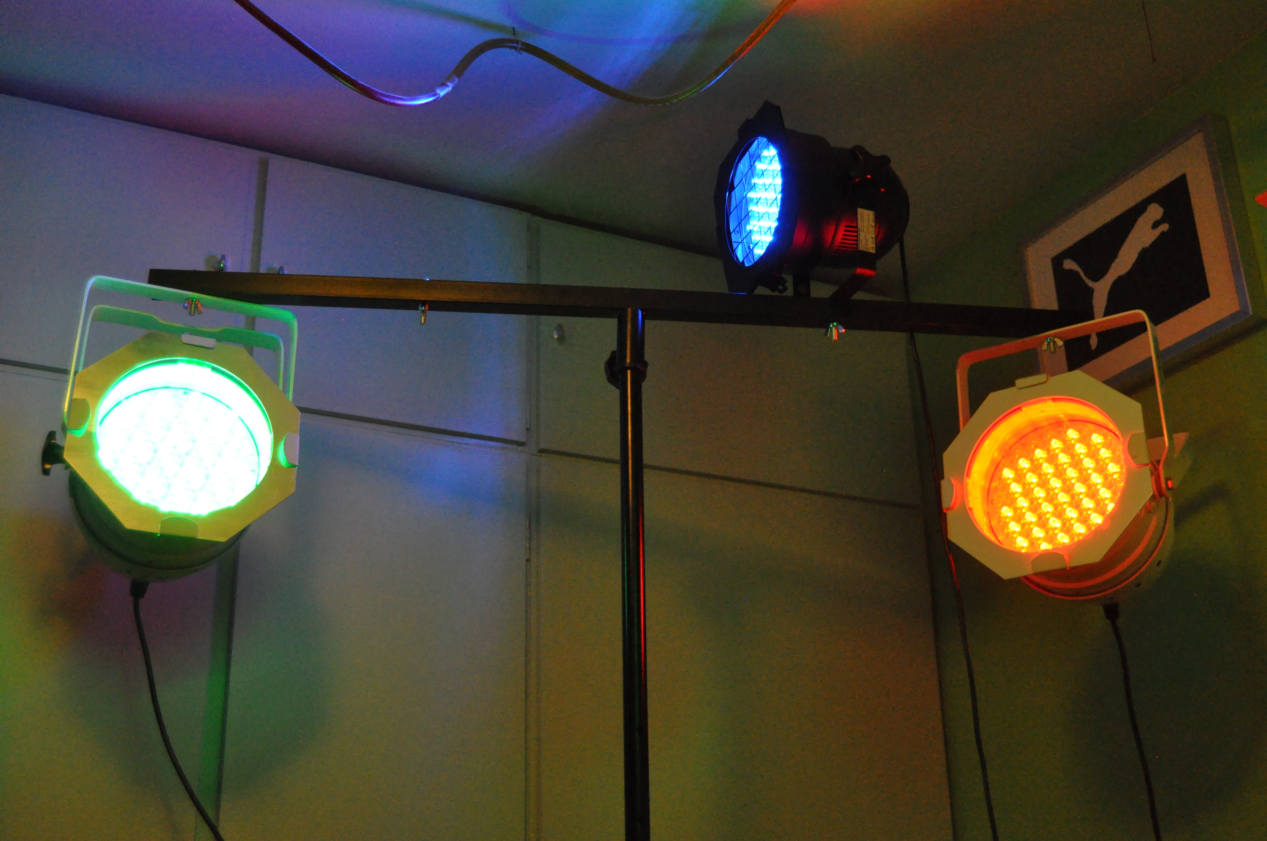 Een statief met 3 PAR-spot's die aan staan; ze zijn ingesteld op de drie in verschillende kleuren (rood, groen, blauw). We kunnen de LED's zien branden.